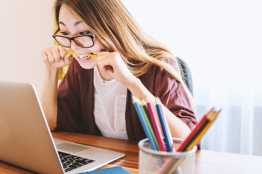 A woman who is visibly stressed sitting at a computer, chewing on a pencil