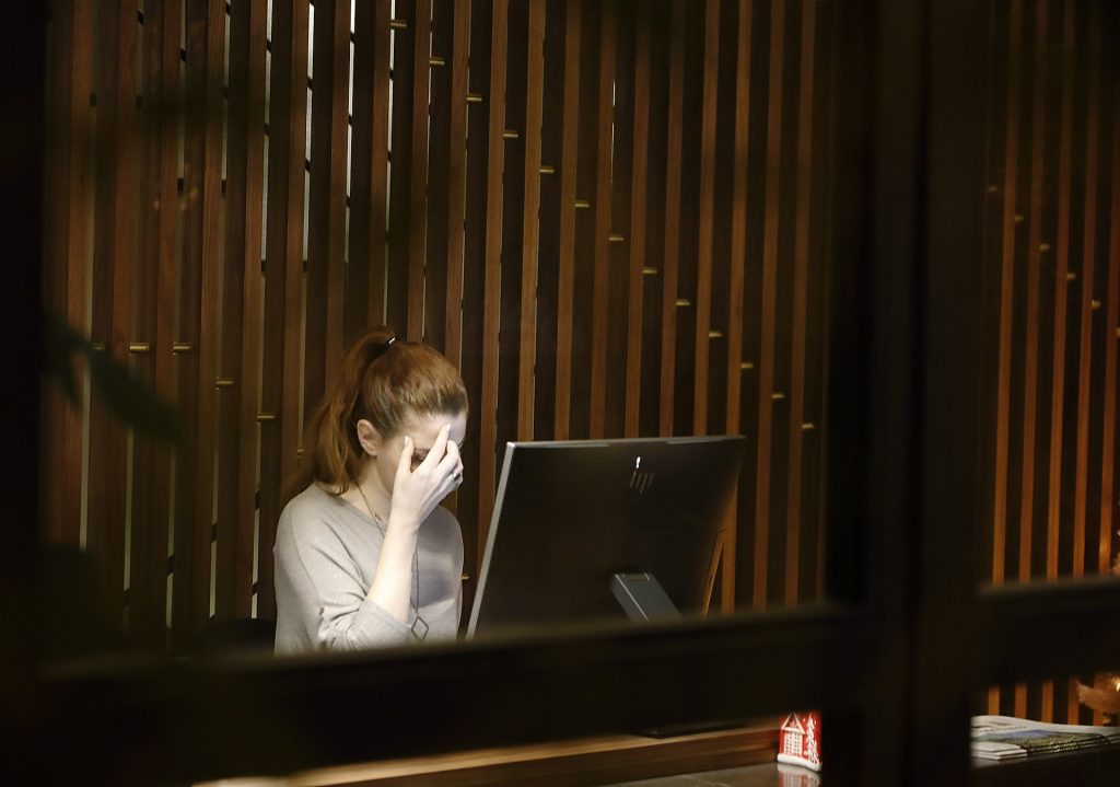 Photo of a woman with her head down, sitting in front of a computer